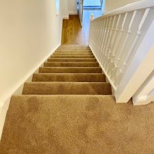 View down a flight of stairs fitted with a polypropylene twist heavy duty domestic carpet in a beige colour, which is moth resistant and bleach cleanable .