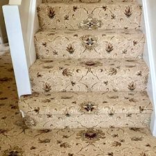 View of a flight of stairs fitted with a high quality traditional woven Axminster carpet with a beige background and medallion design in red and brown.