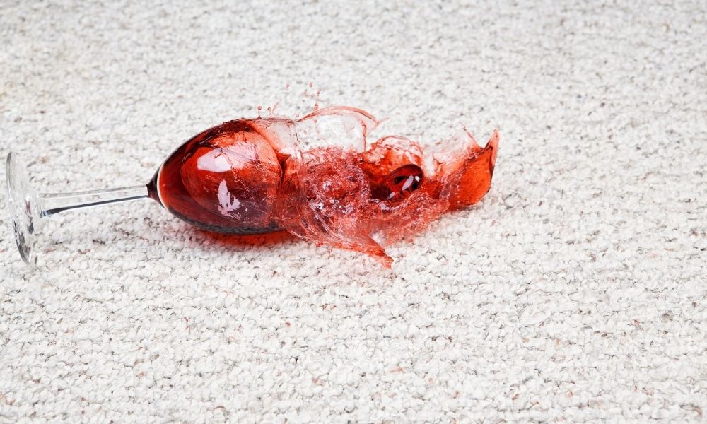 A glass of red wine falling over on a light grey carpet