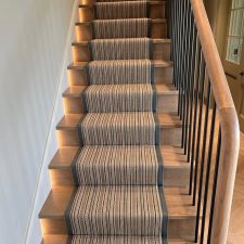 View of a flight of stairs with wooden treads and striped woven runner with B120 leather binding.