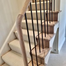 View of a flight of stairs with metal balustrades and wooden bannister, fitted with pale beige wool loop carpet.