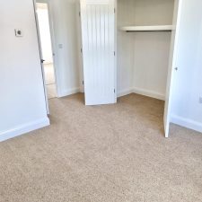 View of a bedroom with white painted walls and a fitted wardrobe cupboard and a beige wool/synthetic quality twist carpet.