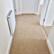 View of a hallway and into bedrooms fitted with a beige twist carpet.