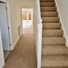 View of a hallway and flight of stairs fitted with a beige twist carpet.