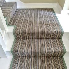 View up a flight of stairs and the midway landing which is fitted with a striped runner in shades of brown, with a 40mm herringbone binding fitted to each edge.