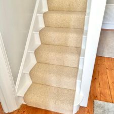 View of a flight of stairs fitted with a beige wool loop pile carpet runner.