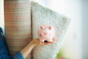Closeup of a lady holding a piggy bank and a roll of carpet to represent the concept of saving money when buying a new carpet.