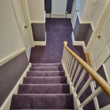 View down stairs into a hallway fitted with a purple nylon twist pile carpet.