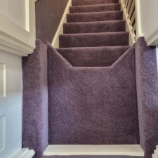 View down stairs into a hallway fitted with a purple nylon twist pile carpet.