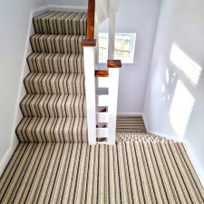 View from an upper landing up and down a flight of stairs fitted with a loop pile, wool/polyester brown and beige striped carpet.