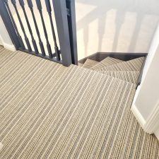 View of an upper landing and down a flight of stairs fitted with a striped beige wool loop carpet.