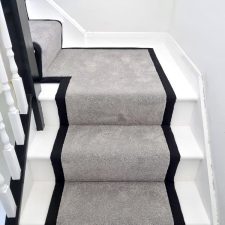 View of a flight of stairs covered with a grey twist pile carpet and 50mm of herringbone binding to the sides.