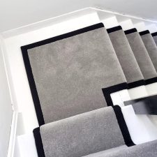 View down a flight of stairs covered with a grey twist pile carpet and herringbone binding to the sides.