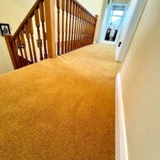 View of a landing fitted with a mustard coloured wool twist carpet.