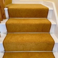 View of a stair treads fitted with a mustard coloured wool twist carpet runner with chrome stair rods.