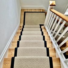 View down a flight of stairs fitted with a herringbone-patterned cream carpet with black binding and black rods.