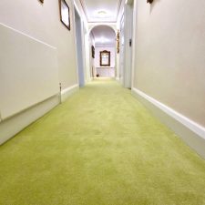 A long corridor fitted with a light green plain carpet.