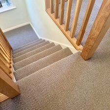 view down a flight of stairs fitted with a neutral colour wool loop pile carpet in a herringbone design.