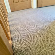 Closeup view of a landing fitted with a neutral colour wool loop pile carpet in a herringbone design.