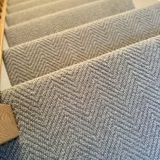 Close-up view down a flight of stairs fitted with a neutral colour wool loop pile carpet in a herringbone design.
