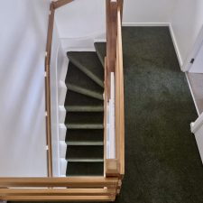 View of a landing and down a flight of stairs fitted with green twist pile carpet fitted as a runner with colour matching whipped edges.