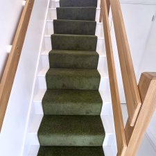 View up a flight of stairs fitted with green twist pile carpet fitted as a runner with colour matching whipped edges.